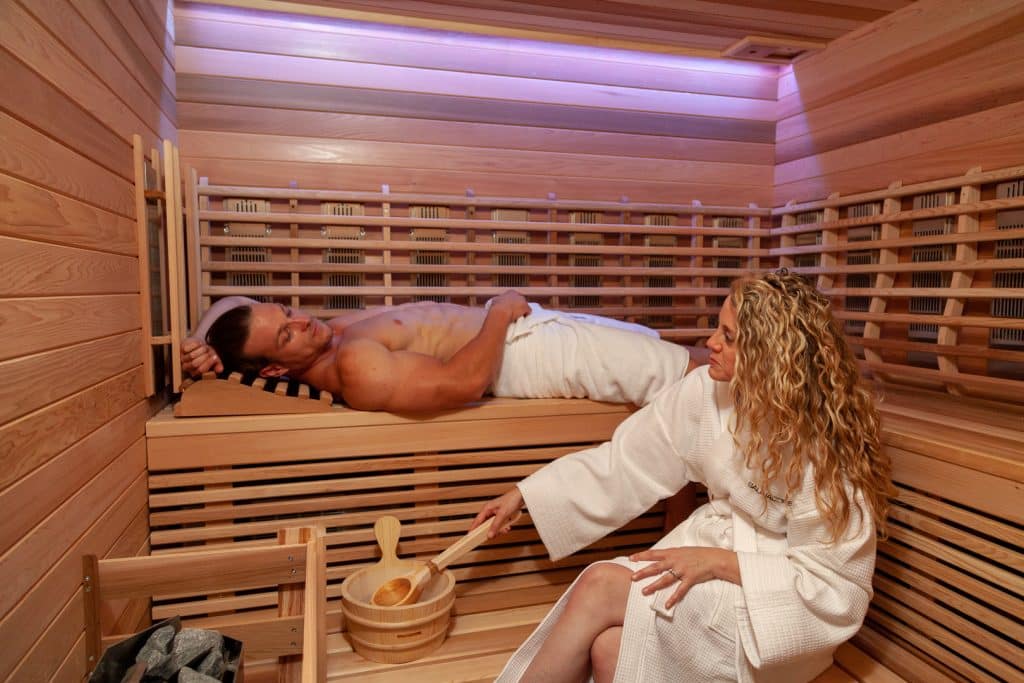 Couple relaxing in wood sauna while wearing white robes